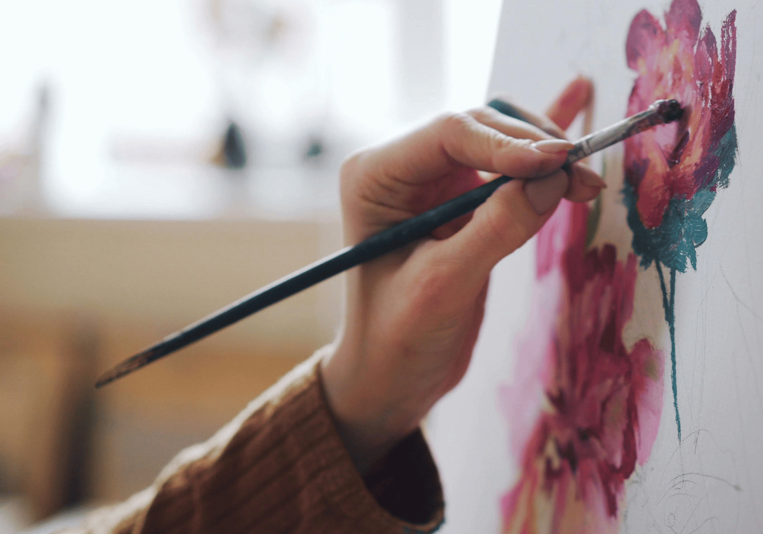 Person painting pink flowers on a canvas with a brush close up of the hand and brushstrokes in focus