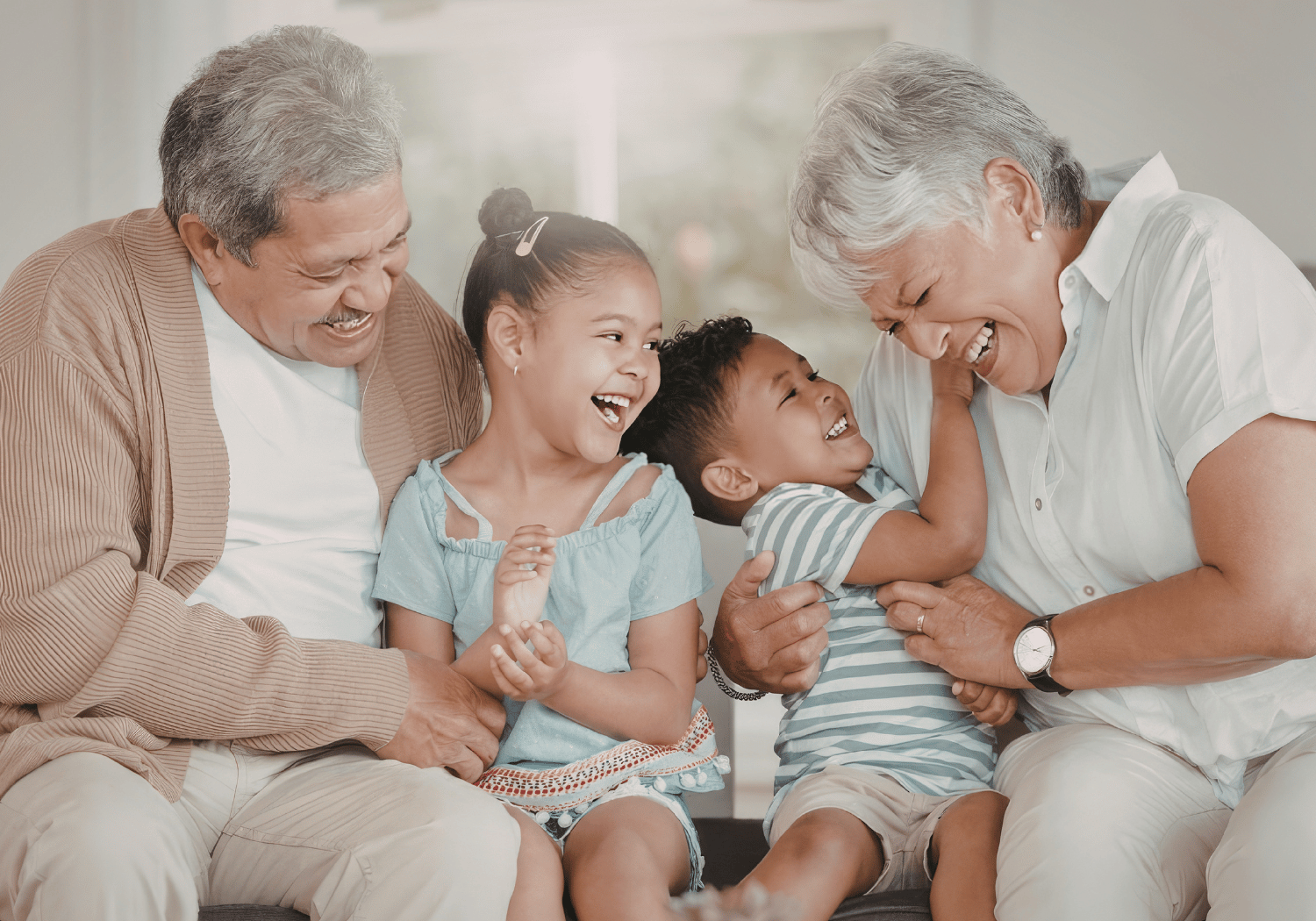 Grandparents laughing with two young children on a sofa, sharing a joyful moment.
